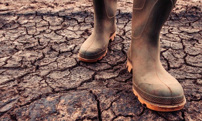farmer-in-rubber-boots-standing-on-dry-soil-ZW42BYM.jpg